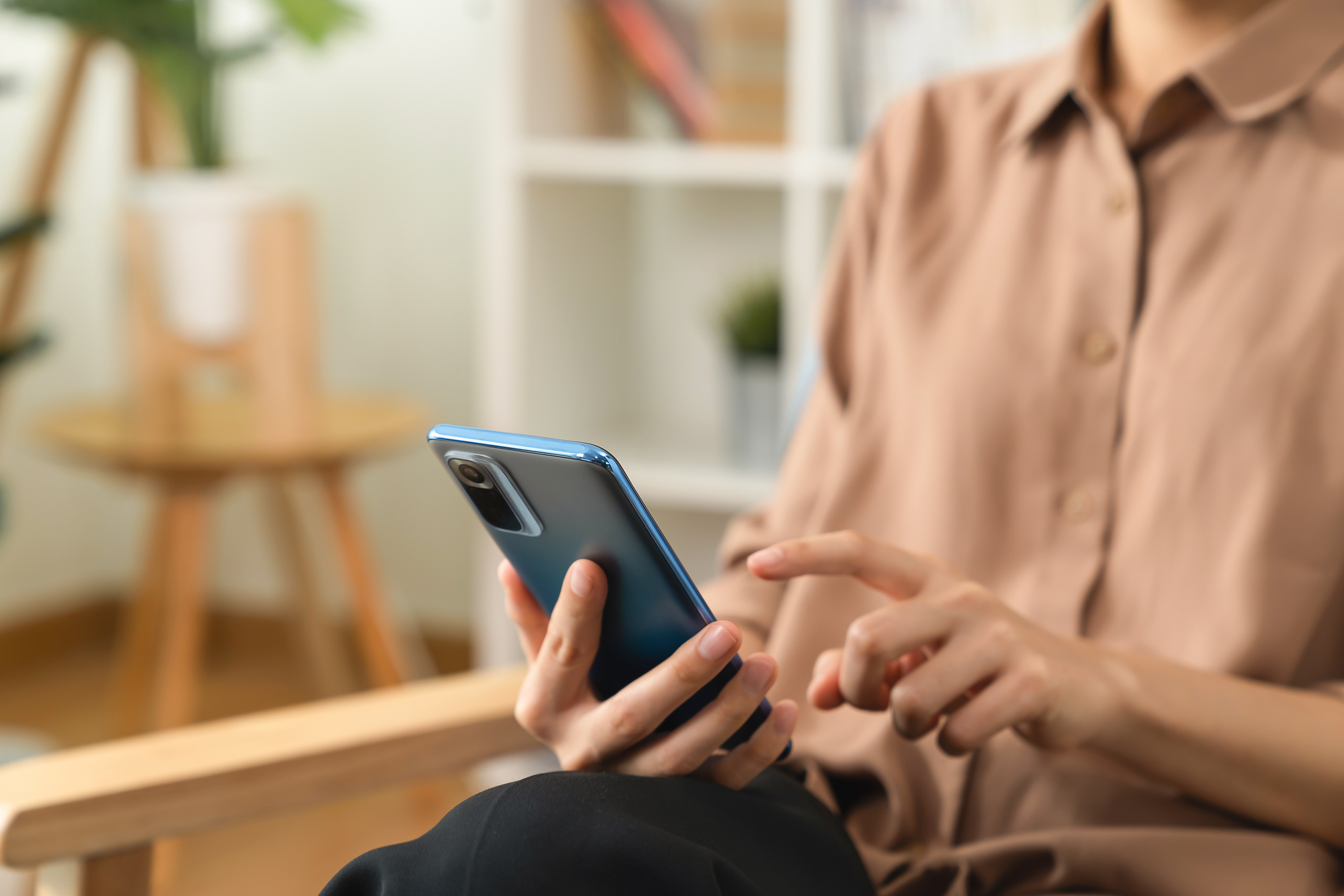 Hand holding smartphone with using social media on internet on sofa in living room.